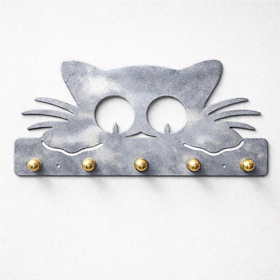 Heated gray metal cat-shaped wall key holder with brass hooks on neutral wall