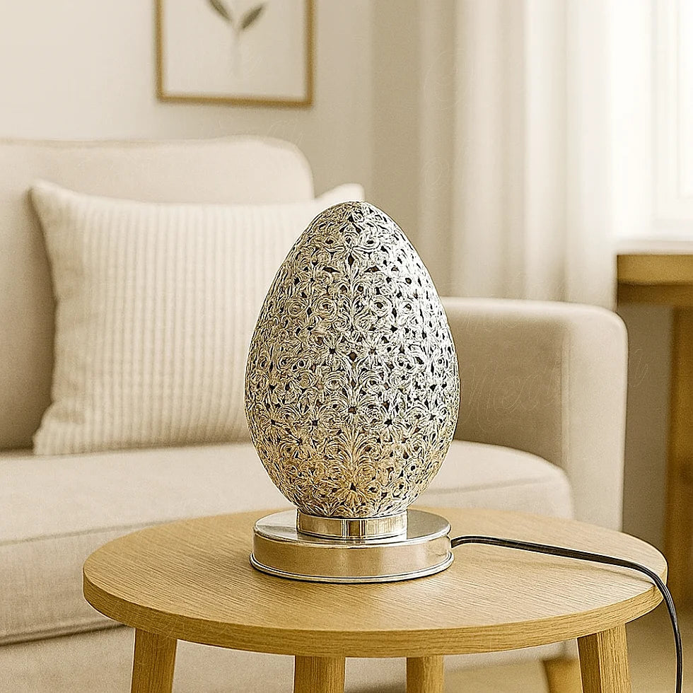 Small Moroccan silver egg-shaped lamp on a wooden table in a bright European living room with natural light and minimalist decor.