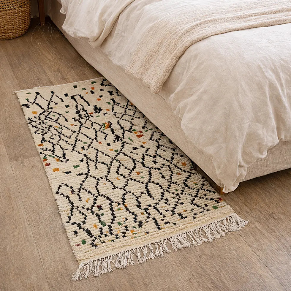 Handcrafted Boujaad Azilal Berber rug in natural wool, black linear motifs with colorful symbols, used as a bedside rug