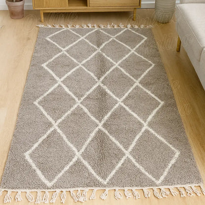Alfombra de lana gris con líneas de rombos blancos y flecos claros, situada entre un sofá y un sillón