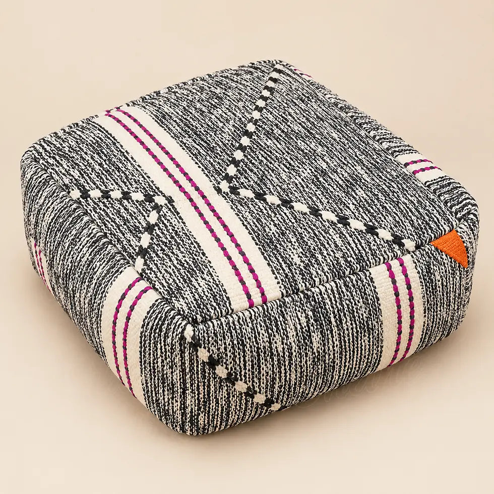 Pouf carré en laine chinée noire et crème, avec bandes fuchsia et détail orange, sur fond beige