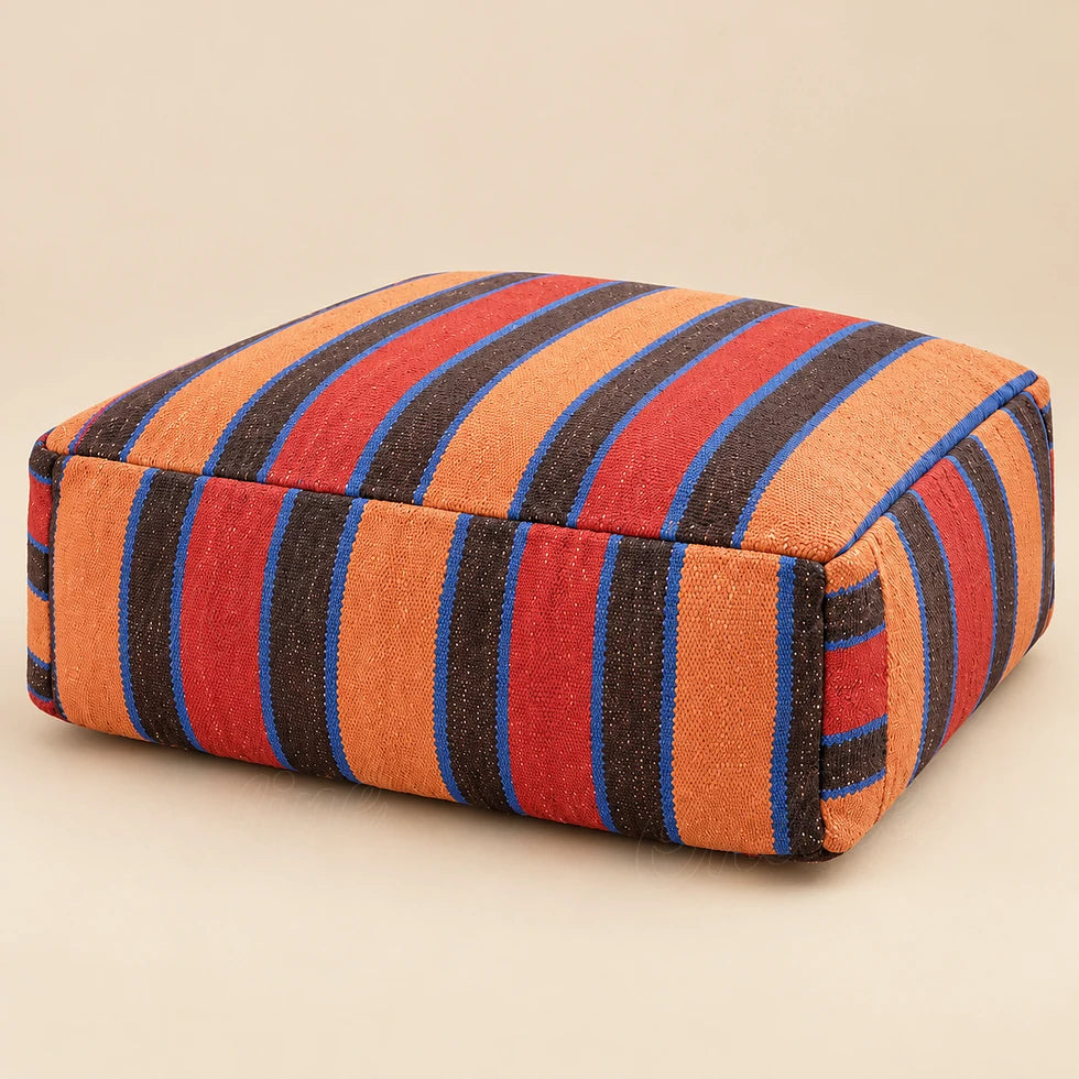 Square wool pouf with wide red, orange and brown stripes and thin blue lines on a beige background