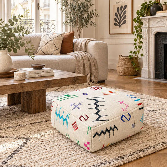 Ivory wool pouf with colorful geometric motifs in a living room with a light sofa and carved fireplace