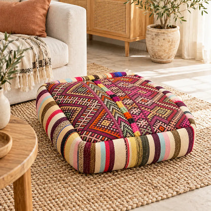 Pouf en laine bordeaux à motifs géométriques multicolores près d’une fenêtre