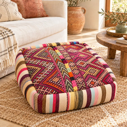 Pouf en laine bordeaux à motifs géométriques multicolores près d’un canapé