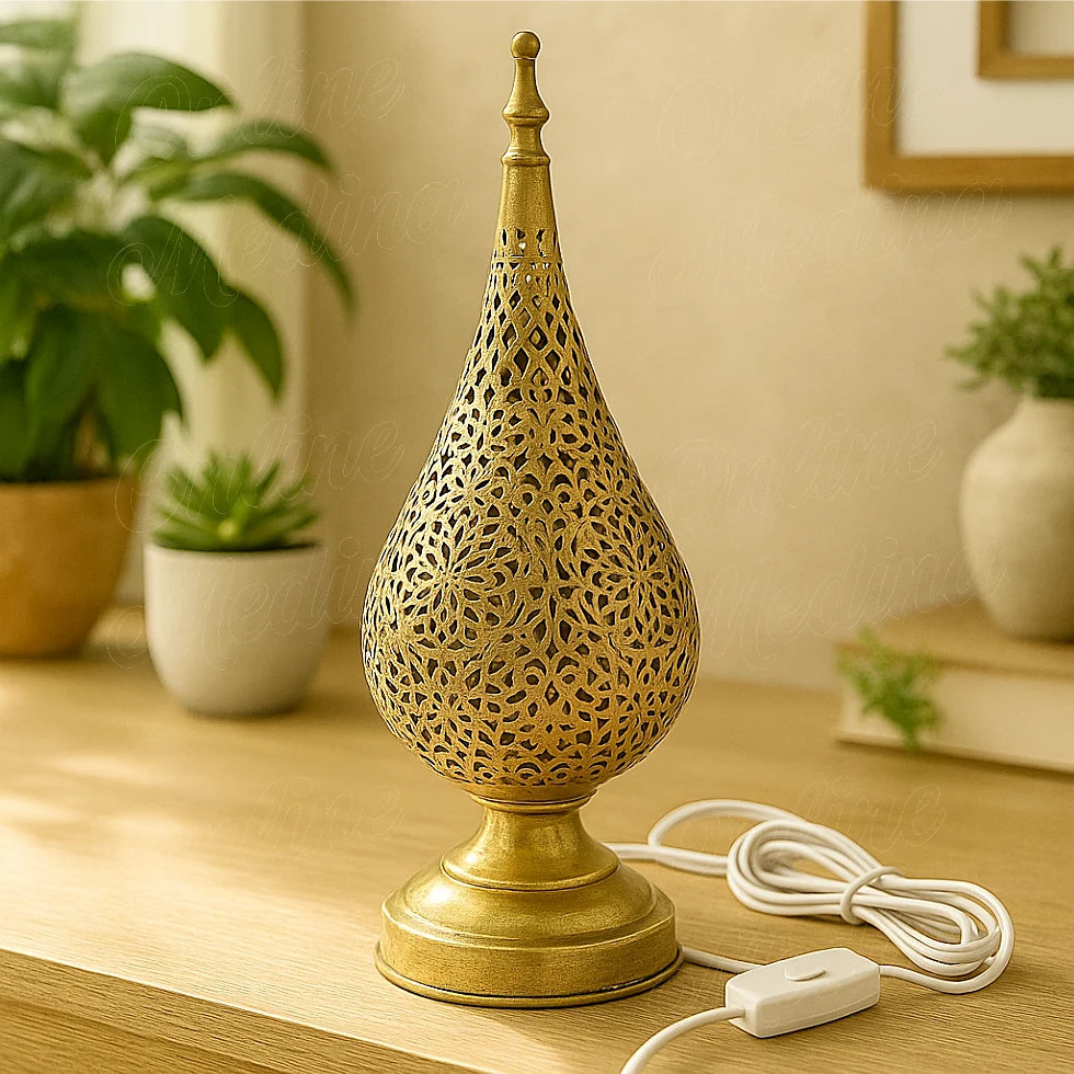 A handcrafted Moroccan tear-shaped brass table lamp with floral perforations, placed on a wooden surface in a modern living room.