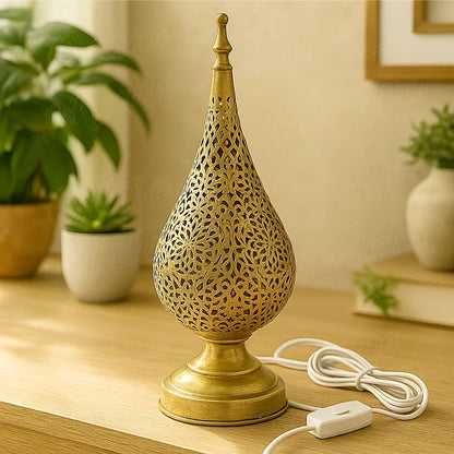 A handcrafted Moroccan tear-shaped brass table lamp with floral perforations, placed on a wooden surface in a modern living room.