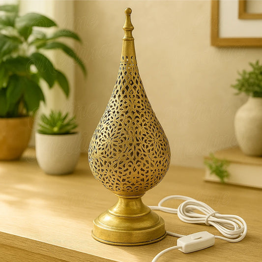 A handcrafted Moroccan tear-shaped brass table lamp with floral perforations, placed on a wooden surface in a modern living room.