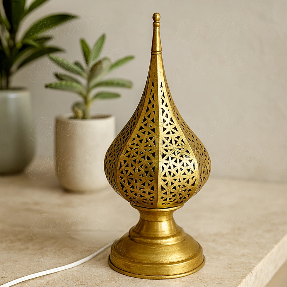 A small golden Moroccan lamp with geometric cutout patterns, displayed on a stone surface in a minimalist home setting.