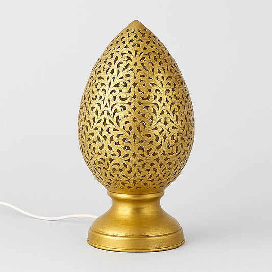 Flame-shaped openwork metal lamp, gold-colored finish, on a pale background with its power cord.