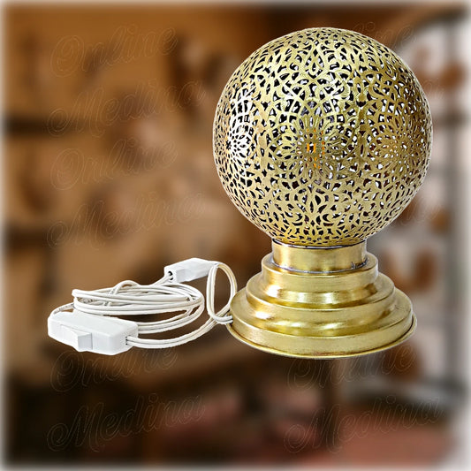 Handcrafted Moroccan table lamp in polished brass, shaped like a pierced globe, featuring intricate floral cutouts and mounted on a wide base – traditional craftsmanship from Marrakech, ideal for soft ambient lighting.