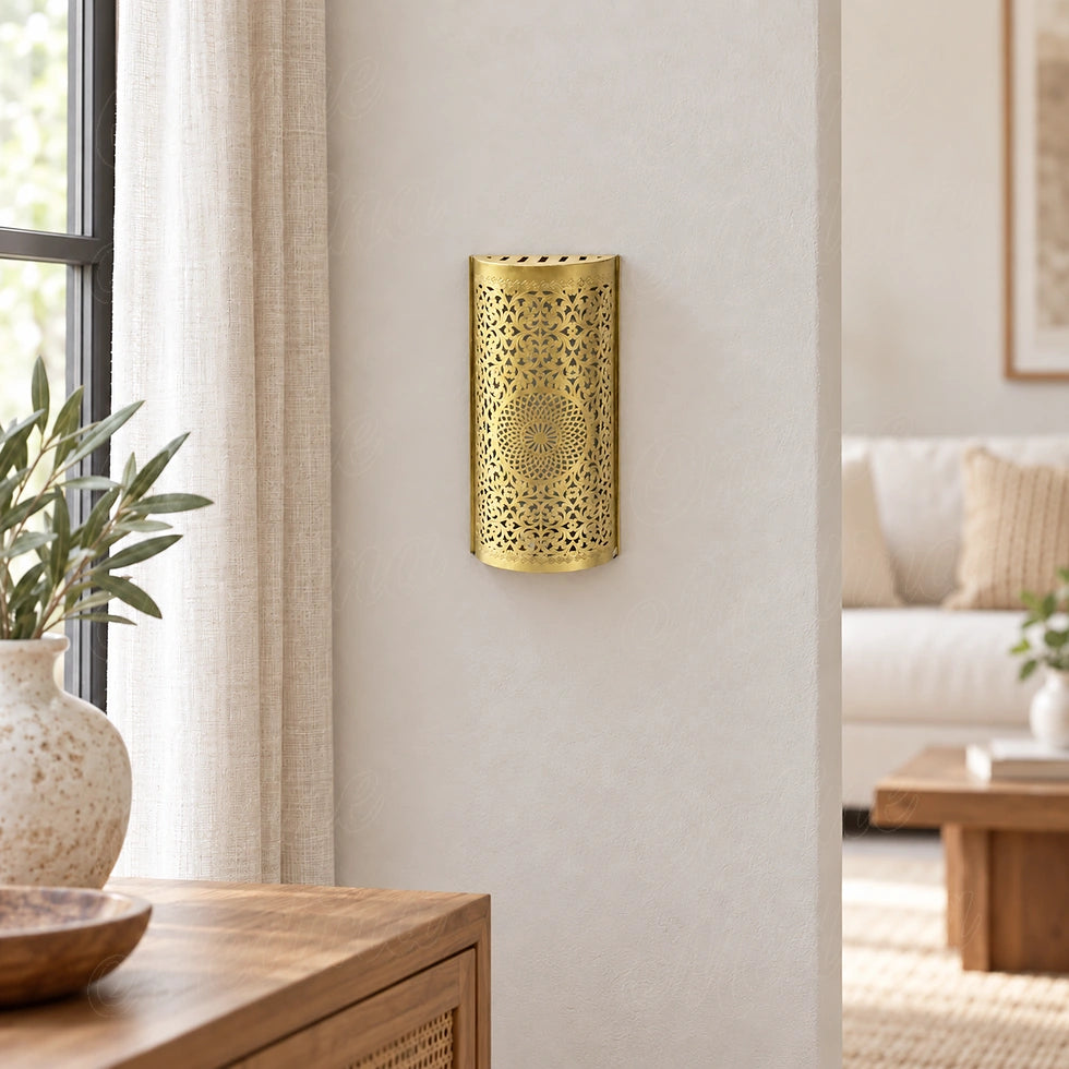 Aplique de pared de metal calado, acabado dorado, sobre una pared junto a una ventana.