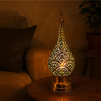Lit Moroccan brass candle lantern glowing warmly through its oriental patterns at night.