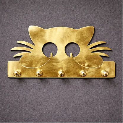 Brass cat-shaped wall key holder on light wall with round brass hooks