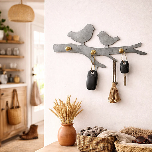 Wall-mounted bird key holder in heated galvanized metal with brass hooks, shown in a warm and realistic home entryway interior