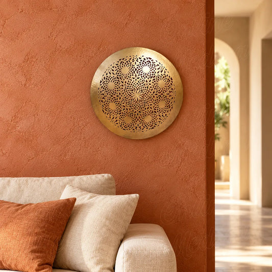 Close view of a round brass wall sconce with openwork floral rosettes on a terracotta wall above a sofa.