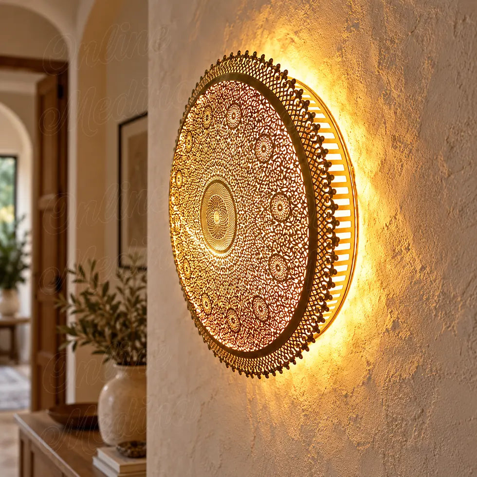 Round brass wall sconce with openwork floral rosettes, seen from the side with warm light on a cream wall.