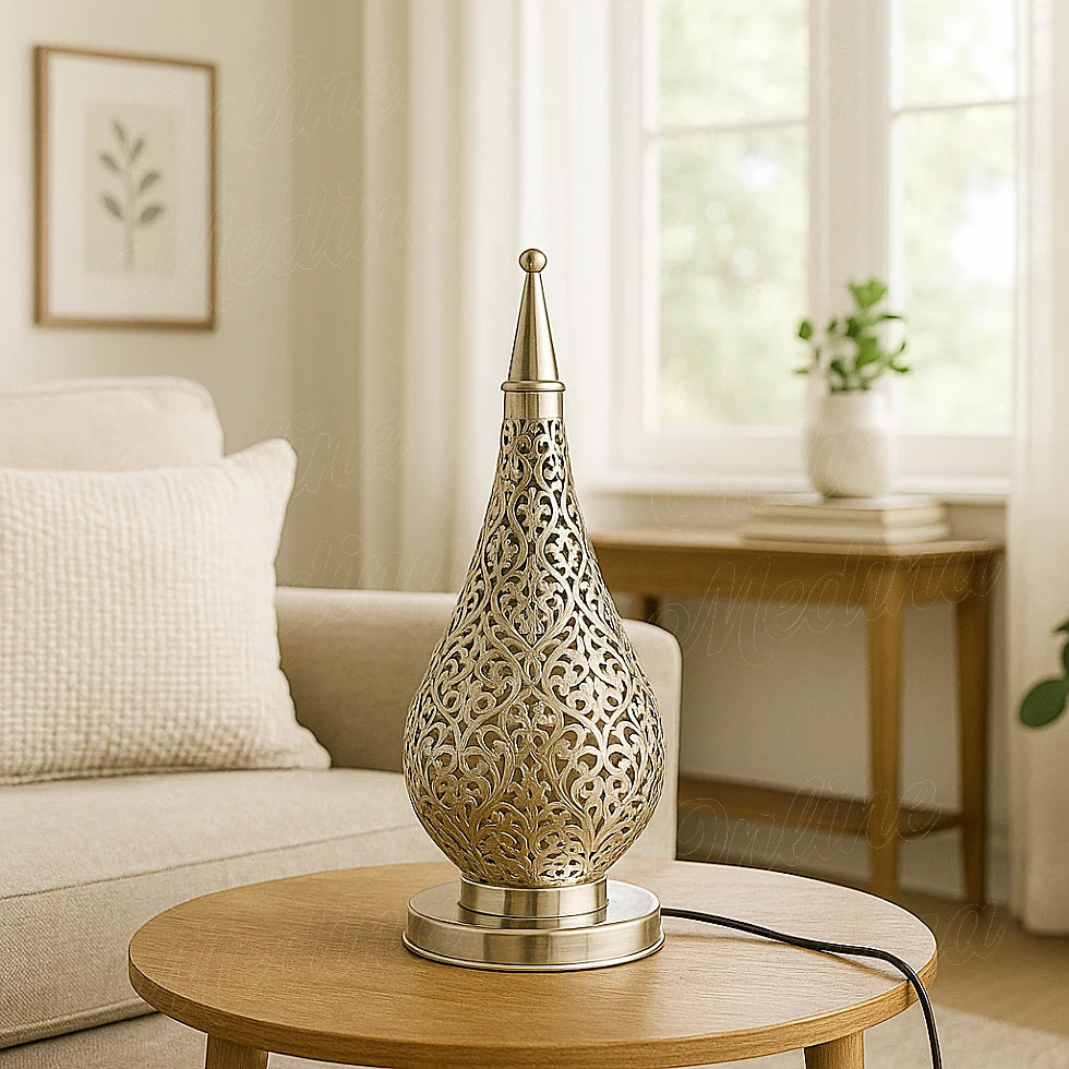 Moroccan silver drop-shaped lamp on a small wooden table in a bright modern living room with beige tones and soft natural light.