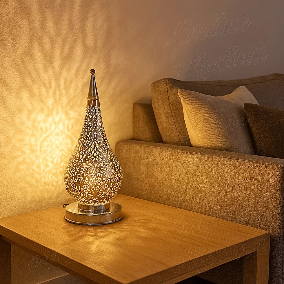 Large Moroccan silver floor lamp beside a light beige sofa in a bright minimalist living room, unlit and reflecting daylight from the window.