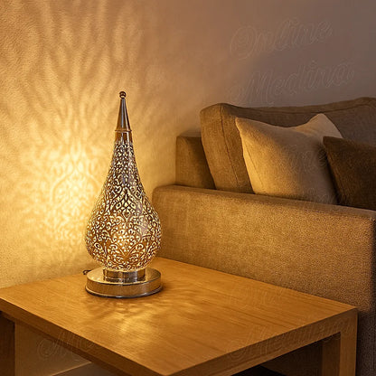 Large Moroccan silver floor lamp beside a light beige sofa in a bright minimalist living room, unlit and reflecting daylight from the window.