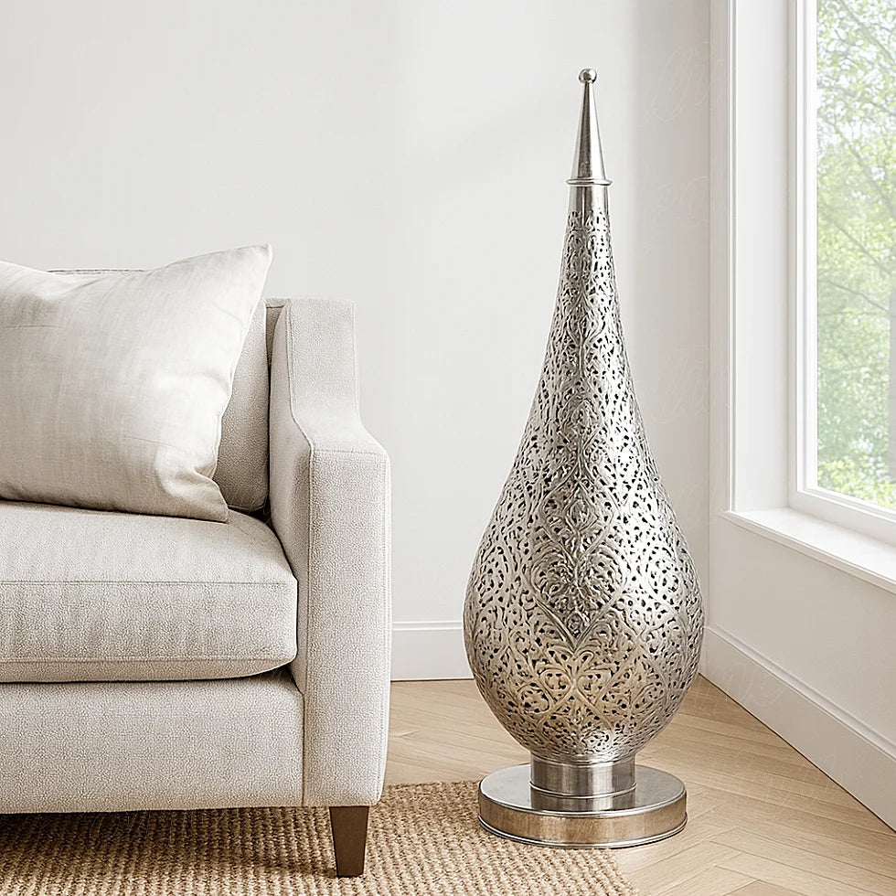 Silver Oriental pierced metal lamp lit up on a wooden side table beside a beige sofa, creating warm light and shadow patterns on the wall.
