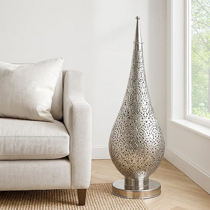 Silver Oriental pierced metal lamp lit up on a wooden side table beside a beige sofa, creating warm light and shadow patterns on the wall.