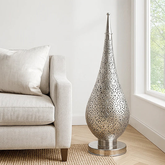 Silver Oriental pierced metal lamp lit up on a wooden side table beside a beige sofa, creating warm light and shadow patterns on the wall.