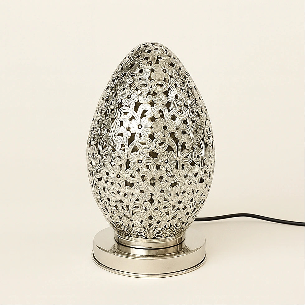 Silver Moroccan egg-shaped pierced lamp with floral patterns and polished base on a plain light background.