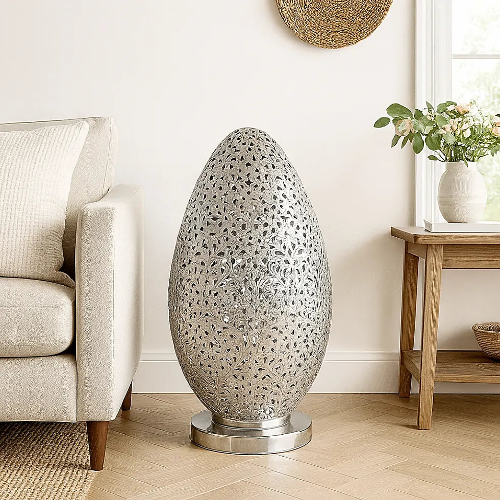 Large Moroccan silver egg-shaped lamp placed on the floor beside a beige sofa in a bright modern living room with wooden furniture.