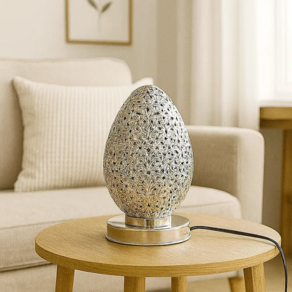 Small Moroccan silver egg-shaped lamp on a wooden table in a bright European living room with natural light and minimalist decor.