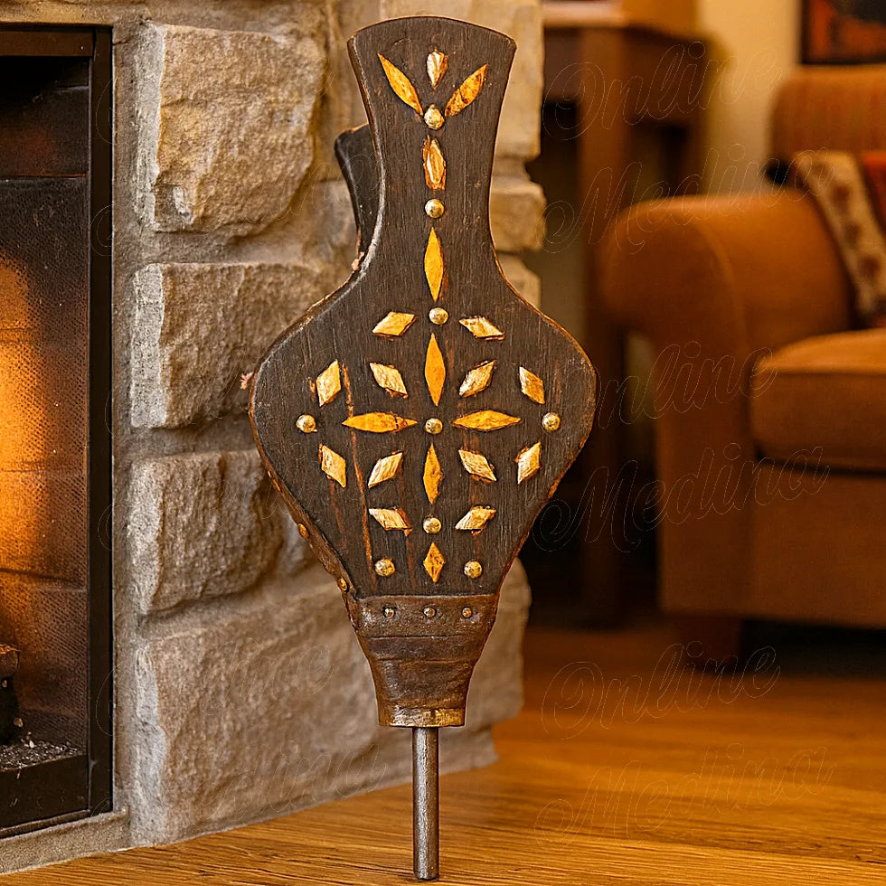 Moroccan artisanal bellows made of wood, leather, and bone, placed beside a stone fireplace in a cozy living room