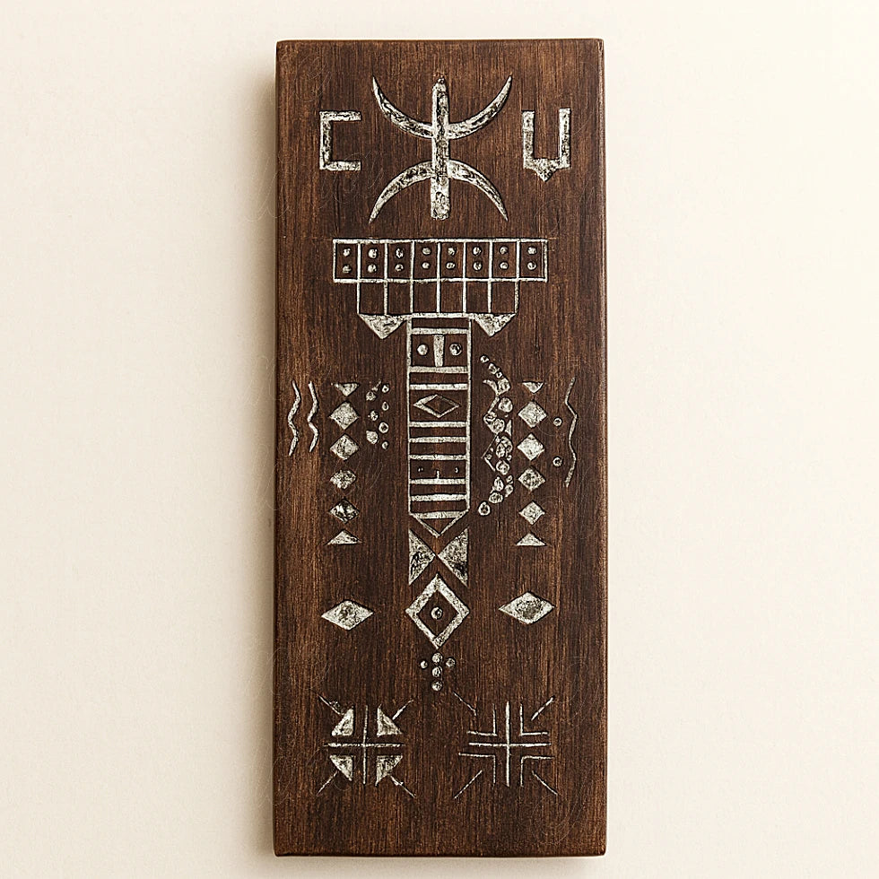 Hand-carved Berber wooden amulet in brown cedar with traditional Amazigh engravings and white patterns, photographed on a light background