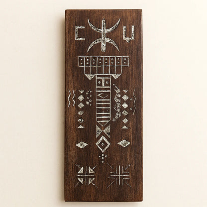 Hand-carved Berber wooden amulet in brown cedar with traditional Amazigh engravings and white patterns, photographed on a light background