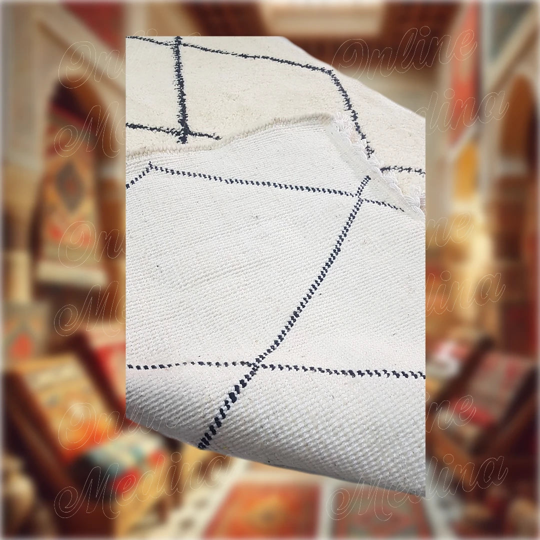 Tapis Beni Ouarain marocain en laine naturelle blanche avec des motifs noirs en losanges. Vue rapprochée montrant l'envers du tapis et ses détails tissés à la main.