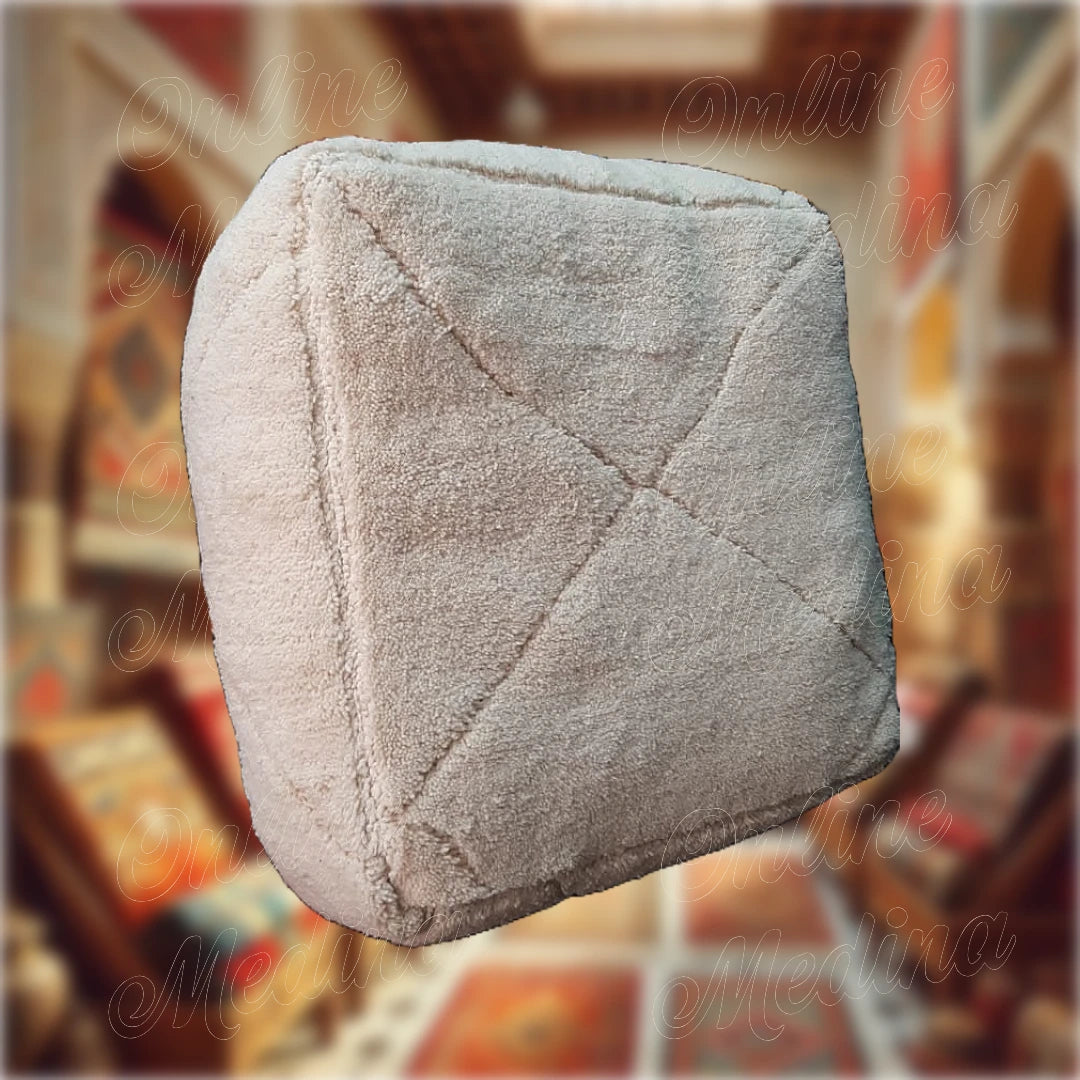 Pouf artisanal marocain en laine beige avec un design uni et minimaliste, fabriqué à la main, parfait pour une décoration moderne et élégante.