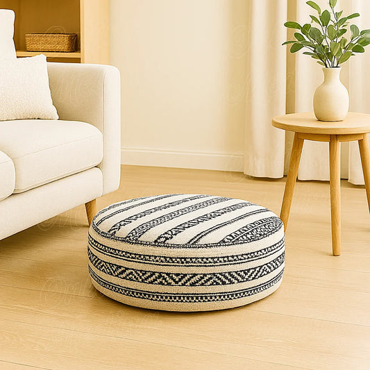 Moroccan Berber round pouf in black and white woven wool, handmade in Rabat, placed beside a beige sofa and wooden table in a bright European living room.