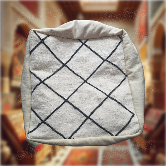 Square Berber pouf in natural wool with black diamond motifs on a cream white background, handmade for cozy and minimalist interiors.