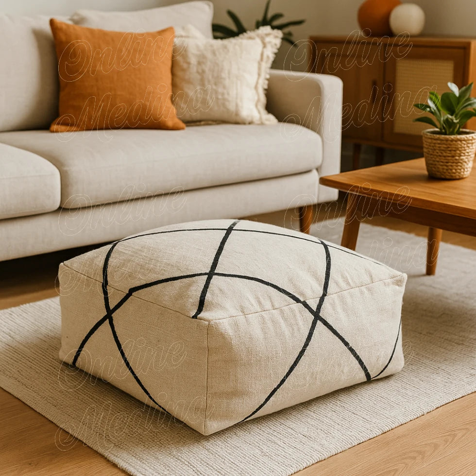 Square Moroccan pouf in natural wool with black diamond pattern, handmade by artisan Omtad in Rabat, placed in a bright living room
