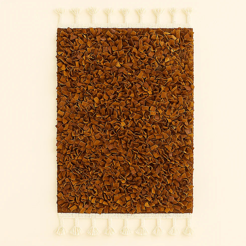 Handwoven brown Moroccan boucharouite rug made from soft recycled leather strips, with white fringes on both ends, photographed on a neutral background.