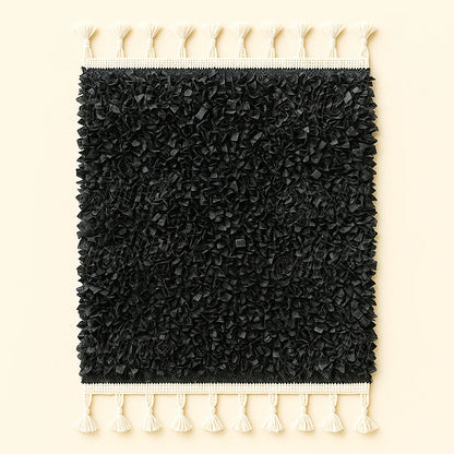 Black Moroccan boucharouite rug crafted from soft recycled leather strips with white fringes, photographed on a plain beige background.